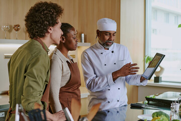Professional Indian chef showing salad picture from new menu to his young biracial cooks