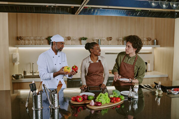 Team of professional chefs of different age choosing ingredients to cook salad