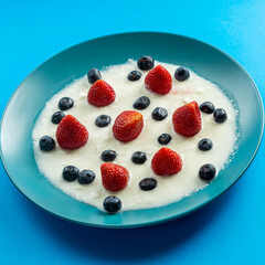 Fresh juicy berries strawberries and blueberries in a blue plate with thick whipped cream