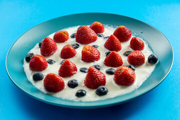 Berries juicy strawberries and blueberries in a blue plate with cream on a blue background, top view