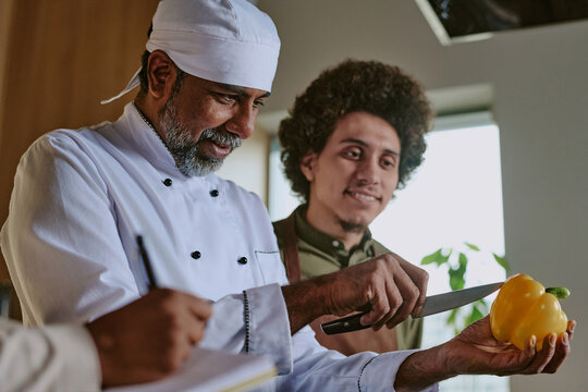 Low angle shot of Indian professional chef showing peeling skills to his intern
