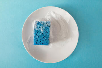 Cleaning sponge with soap on a white plate on a blue background. top view