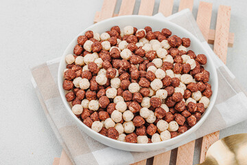 Vegan cereals in balls shape of cocoa and vanilla served with spoon. Full bowl ready to eat