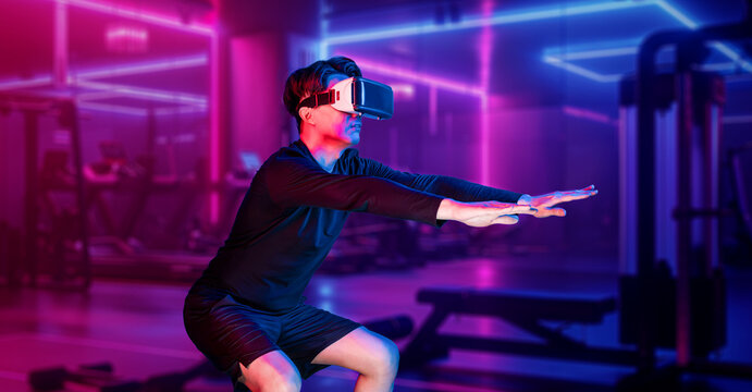 Asian man wearing VR glass while exercising at futuristic gym with glowing vibrant color. Male model using augmented reality technology for analysis data. Technology innovation concept. Ingenuity.