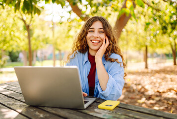 Young woman brought her laptop to the park to get some fresh air and work. Online education, Freelance work, technology concept.