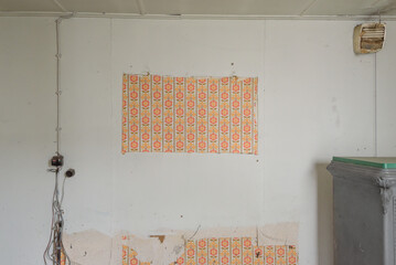 Empty abandoned room with pieces of floral wallpaper and electrical components