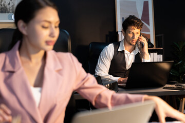 Focusing businessman calling with customer for creative business project planning at back view at night light modern office with fronted view blurry secretary checking paperwork report. Postulate.