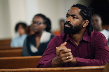 African american man praying and listening to sermon in church pew