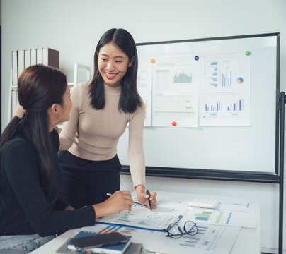 Collaborative Growth: A dynamic duo of female business professionals huddle over financial data, showcasing their commitment to achieving success together.