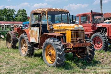 An abandoned tractor sits in a field, overgrown with weeds