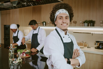 Medium close up portrait of young curly haired sous chef smiling widely while posing for photo