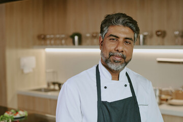 Portrait of confident Indian chef posing for photo in spacious kitchen