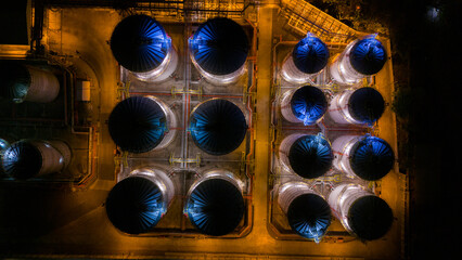 Aerial night view of a symmetrical industrial complex with illuminated cylindrical structures casting an enigmatic glow