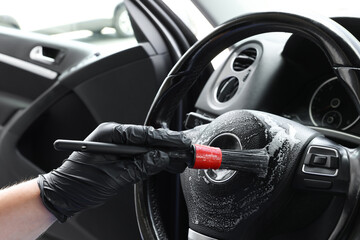 Man cleaning steering wheel with brush in car, closeup