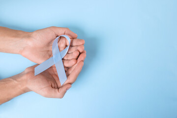 Prostate cancer awareness. Man with light blue ribbon as symbol of support on color background, top...