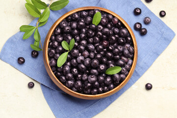 Ripe acai berries and leaves in bowl on light table, flat lay