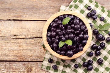 Ripe acai berries and leaves in bowl on wooden table, top view. Space for text
