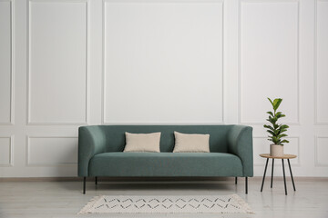 Stylish sofa, pillows and side table with houseplant near white wall indoors