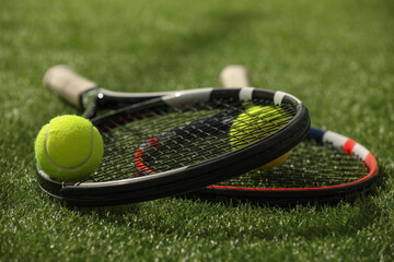 Tennis rackets and balls on green artificial grass, closeup