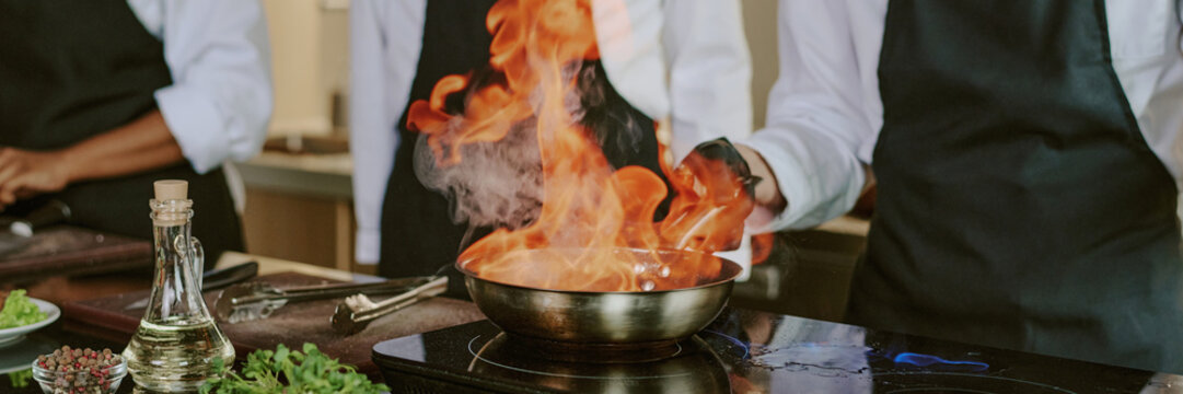 Header of unrecognizable sous chef cooking flambe steak in professional kitchen