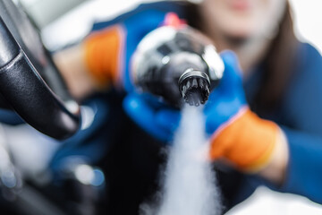 Woman cleaning car interior with spray cleaner while wearing gloves in a bright workshop setting