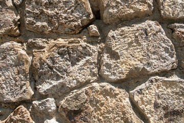 Close-up view of weathered stone wall featuring uneven textures and natural colors in sunlight