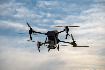 Fototapeta premium Large agricultural drone in flight, fertilizing a sown field.