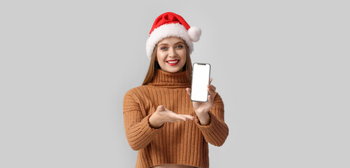Beautiful young woman in Santa hat and with mobile phone on grey background