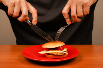 Man holds burger with hands. Man eats homemade beef burger on wooden table. Ready to eat tasty fast food hamburger. Unhealthy food concept. Home delivery. Close up shot of young man eats burger.