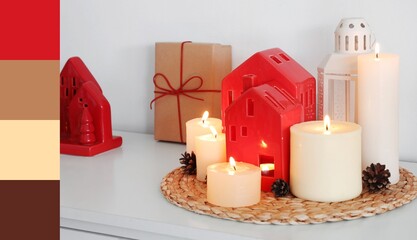 Burning candles with house shaped holders and Christmas gift on shelf in room. Different color patterns