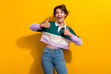 Portrait of pretty nice young girl astonished show thumb up wear shirt isolated on yellow color background