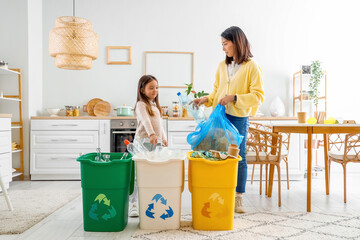 Asian mother with her little daughter sorting garbage with recycle bins in kitchen