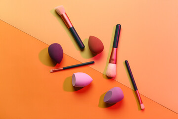 Makeup sponges and brushes on orange background