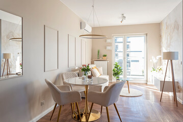 Room interior in new apartment in modern design and decor with wooden floor, table with chair and window. Beige wall with decoration. Real estate.