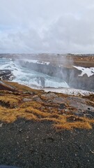 Gullfoss waterfall in nordic landscape, spectacular icelandic scenery with frost and freezing cold water stream running off hills. River flow on top of frozen hilltop, majestic arctic waterfall.