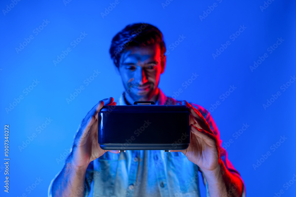 Poster smiling caucasian man holding and show vr headset with blurring background while standing with neon 