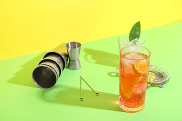 Glass of cold Negroni cocktail, ice cubes and bartender tools on color background
