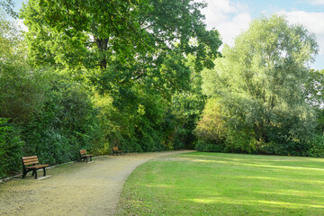 View of beautiful park with benches, green grass and trees
