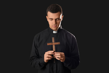 Young priest with cross on dark background