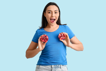 Beautiful young woman with fresh pomegranate on blue background