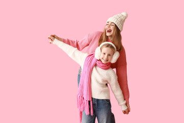 Happy little girl and her mother in winter clothes on pink background