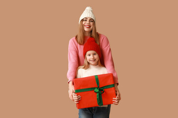 Cute little girl and her mother with Christmas gift box on brown background