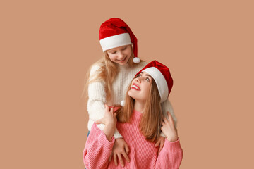 Cute little girl and her mother in Santa hats on brown background