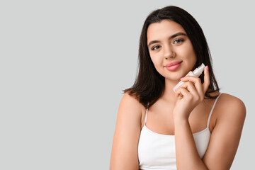 Fototapeta premium Beautiful young woman holding bottle of cosmetic product on grey background