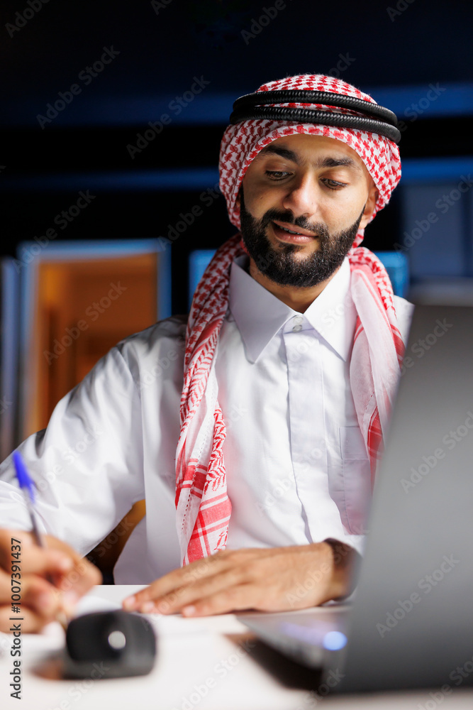 Poster detailed view of arab man working efficiently at the workplace by surfing the internet and writing n