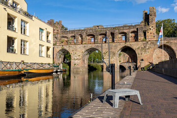 Historic facades of medieval city wall ruins of the Berkelpoort boat entrance in the background and reflecting in the water against blue sky with clouds