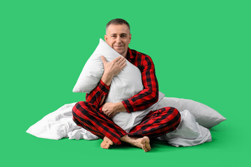 Handsome mature happy man in checkered pajamas with pillow and blanket on green background