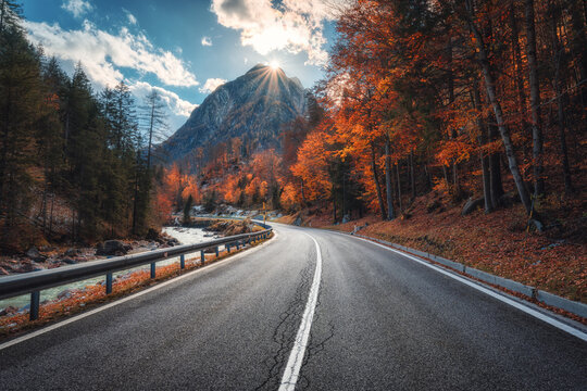 Winding mountain road at sunset in autumn. Alps, Italy. Beautiful curved alpine road, snowy rocks, trees, red leaves, blue sky with clouds. Colorful landscape with empty road on mountain pass in fall - Powered by Adobe