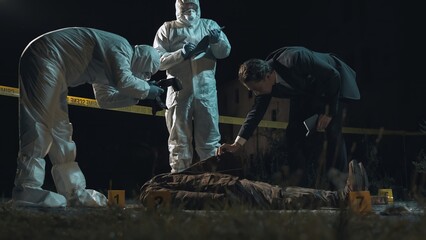 Detective and forensic scientists working hard at crime scene near headless body. Collection and...