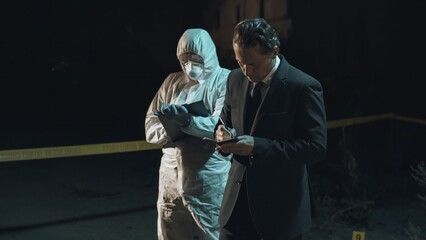 Detective examining main clue brought in by forensic scientist at crime scene, while the rest of...